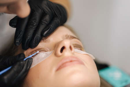 Close-up of eyelash care treatment procedures. Beautiful female, blond hair model have eyelashes lamination. Woman doing staining, curling, laminating and extension for lashesの写真素材