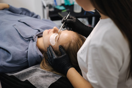 Woman doing eyelashes lamination in beauty studio. Blond hair model has staining, curling,...