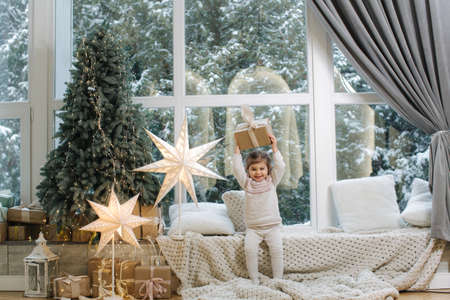 Happy beautiful girl take present in front of big window. Christmas time. Its snow outside. Christmas treeの写真素材