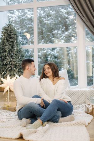 Handsome boy with his beautiful girlfriend hug each other at home at Christmas eve. Fit tree and...