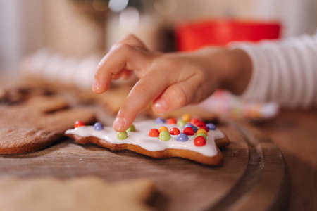 Close-up of little girl in santa hat decorates gingerbread using multicolored beads. Christmas and New Year traditions concept. Christmas bakery. Happy hollidaysの写真素材