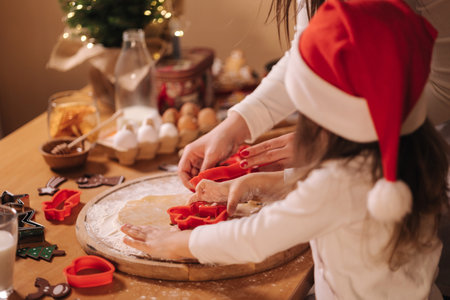 Making gingerbread at home. Little girl with her mom cutting cookies of gingerbread dough. Christmas and New Year traditions concept. Christmas bakery. Happy holidaysの写真素材