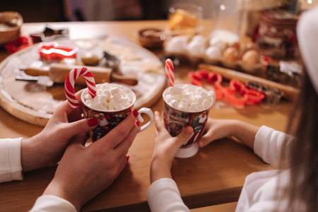Winter drink, white mug with marshmallows in females hands in white sweater. Home bakery, cooking traditional festive sweets. Gingerbread dough on wooden table. New Year celebration traditions. Christmas mood.の写真素材
