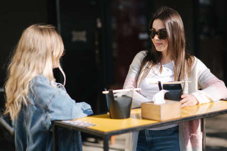 Two beautiful blonde and brunette girls order takeaway chinese food. Young woman outdoors speaking. Spring sunny dayの写真素材