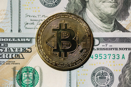 Close-up of golden shiny bitcoin crypto currency coins on one hundred US dollar bills. Difference...