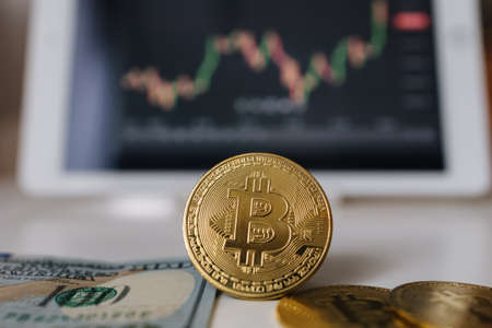 Gold bitcoin crypto currency and US dollars on background of tablet with stock diagram. Investment in virtual money. Cryptocurrency conceptの写真素材