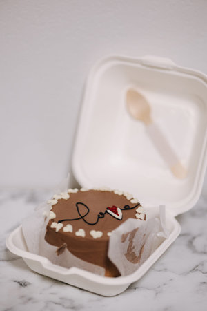 Bento cake with inscription love and white sugar hearts in eco box-packaging with wooden spoon....