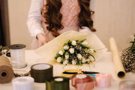 Woman make spring bouquet. Female florist wrapping beautiful bouquet of spring flowers in pack paper on the table. Beautiful flower compositionの写真素材
