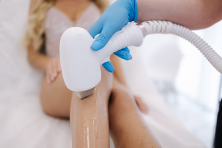 Beautician doing epilation on beautiful womans leg in beauty center. Female receiving laser light...