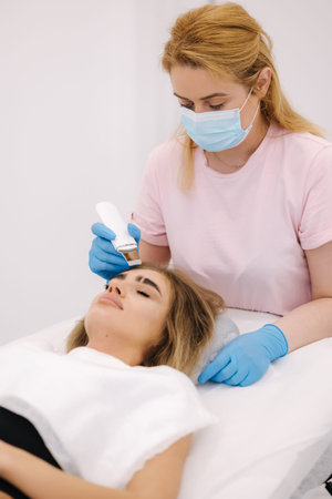 Young woman taking beauty procedure in spa salon. Beautician using peeling device, ultrasonic...