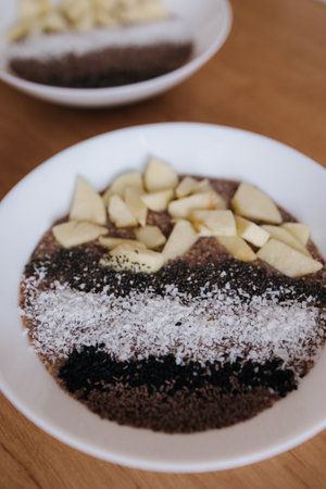 Vegan raw flaxeed porridge with fruits and chia, black sesame and psyllium seeds, coconut flakes. Healthy nutritious and fresh food. Two platesの写真素材