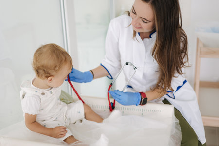 Pediatrician listening infant childs heartbeat with stethoscope during checkup at homeの写真素材