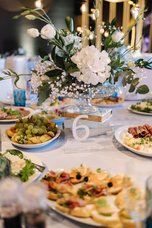 Big round table decorated by white and blue flowers in restaurant. Different dishes on table. Cristening of little boy. Luxury decorの写真素材