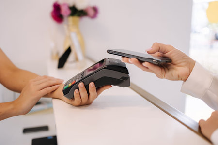 Female customer pay for procedures in beauty studio. Close-up of woman pay using phone and put to...