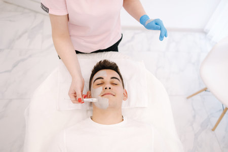 Handsome man having cosmetic mask in beauty studio. Top view of male in spa salon