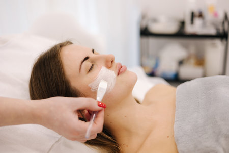 Cosmetologist applying clay mask on womans face in spa salon. Side view of male face during procedure.の写真素材