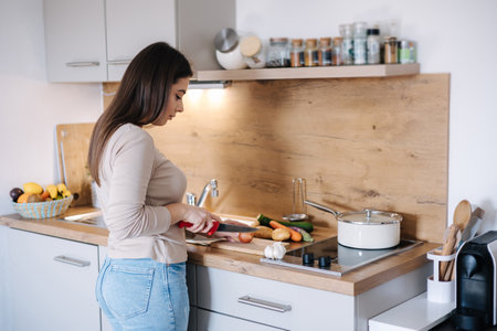 Back view of young beautiful woman is preparing lunch in her kitchen at homeの写真素材