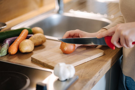 Side view of woman cutting an onion on a wooden board. Home food conceptの写真素材