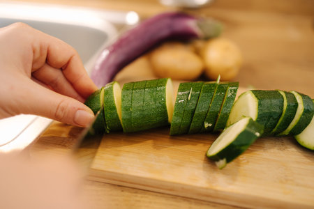 First person view of female hand cutting green zucchini on wooden table at the kitchen. Home food conceptの写真素材