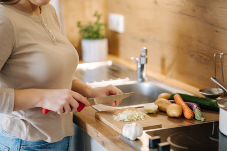 Woman is cutting onions on wooden boards and is preparing to pour them into a frying panの写真素材