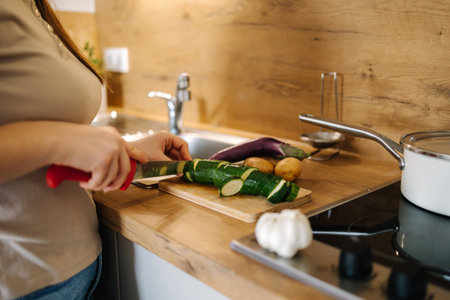Close-up of woman cutting zucchini on a wooden board. Home food concept
