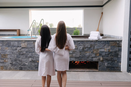 Back view of two pretty woman in white robe preparing for hot tube bathing. Relax outdoor in luxury resortの写真素材