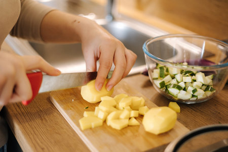 Close-up of female cutting potato on wooden board at home. Home made food conceptの写真素材