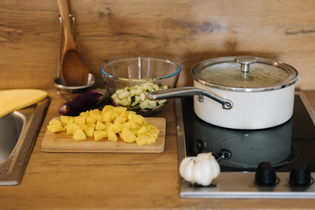 Chopped vegetables on a wooden board. Potato and zucchini prepared for cooking. White saucepan on electric burnerの写真素材