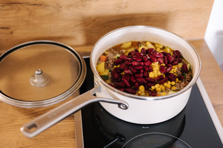 Different vegetables with forcemeat, corn and red beans in white saucepan on kitchen. Mexican traditional foodの写真素材