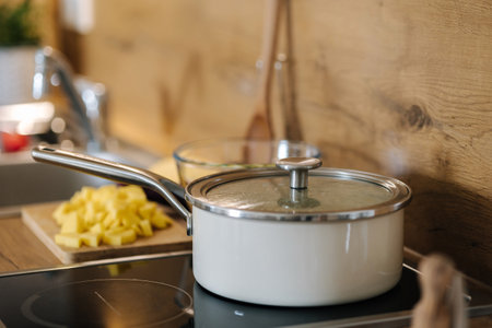 Chopped vegetables on a wooden board. Potato and zucchini prepared for cooking. White saucepan on electric burnerの写真素材