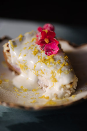 A piece of cheesecake with sweet cream sauce and lemon zest, decorated with an edible pink flowerの写真素材