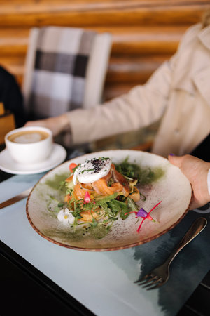 Waiter bring breakfast for customer on terrace. Fresh sandwich with salmon and poached egg on topの写真素材