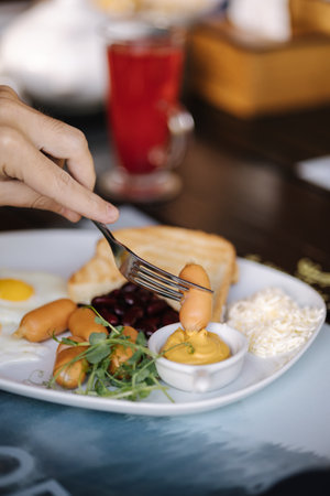 Macro photo of man slice sausage and dips it in mustard. English breakfast outdoor. Lunch in restaurant. Foodの写真素材