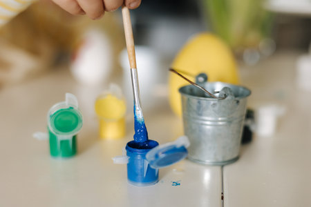 Macro photo of little girl put brush into blue paint. Painting easter eggs. Yellow and blue colour. Ukrainian symbolicの写真素材