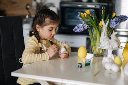 Process of little girl painting eggs on kitchen. Spring holiday. Easter decoration at home. Side viewの写真素材