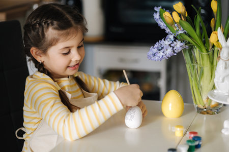 Process of little girl painting eggs on kitchen. Spring holiday. Easter decoration at home. Side viewの写真素材