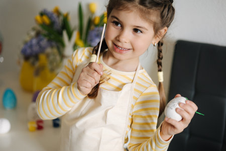 Adorable smiled girl hold brush and eggs in hands and preparing for painting. Easter decoration on kitchenの写真素材