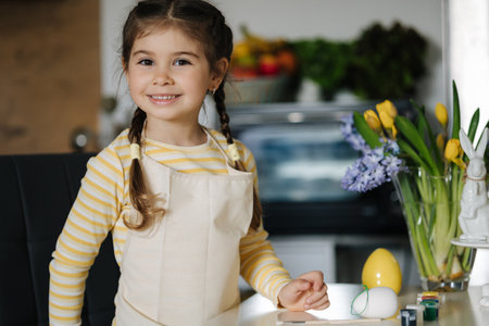 Adorable smiled girl hold brush and eggs in hands and preparing for painting. Easter decoration on kitchenの写真素材