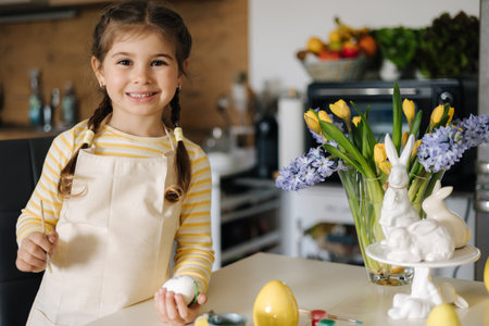 Happy little girl painting easter eggs on kitchen. Cute smiled girl have fun on spring holidayの写真素材