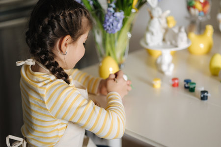 Process of little girl painting eggs on kitchen. Spring holiday. Easter decoration at home. Side viewの写真素材