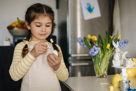 Happy little girl painting easter eggs on kitchen. Cute smiled girl have fun on spring holidayの写真素材
