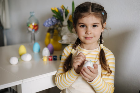 Easter holiday at home. Portrait of adorable little girl painting eggs in kitchen.の写真素材