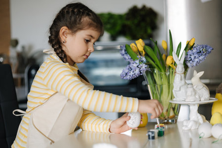 Adorable smiled girl hold brush and eggs in hands and preparing for painting. Easter decoration on kitchenの写真素材