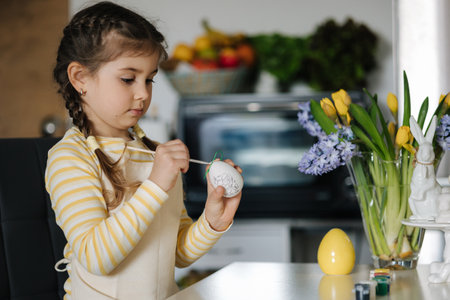 Process of little girl painting eggs on kitchen. Spring holiday. Easter decoration at home. Side viewの写真素材