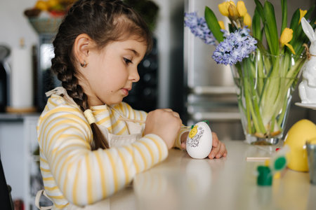 Happy little girl painting easter eggs on kitchen. Cute smiled girl have fun on spring holidayの写真素材