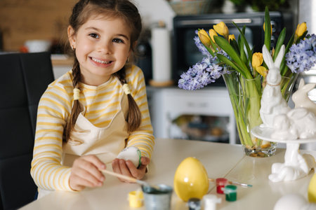 Cute four year girl sitting on kitchen table and painting easter eggs. Yellow and blue colour. Ukrainian symbolicの写真素材