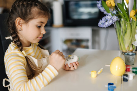 Happy little girl painting easter eggs on kitchen. Cute smiled girl have fun on spring holidayの写真素材
