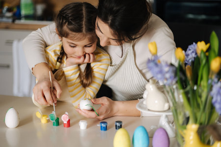 Portrait of mom and daughter painting easter eggs on kitchen. Spring holidays mood. Familyの写真素材