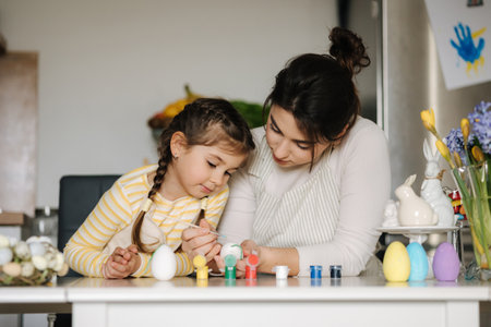 Cute little girl with her mother preparing for painting easter eggs. Mom and daughter in apronの写真素材