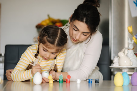 Portrait of mom and daughter painting easter eggs on kitchen. Spring holidays mood. Familyの写真素材